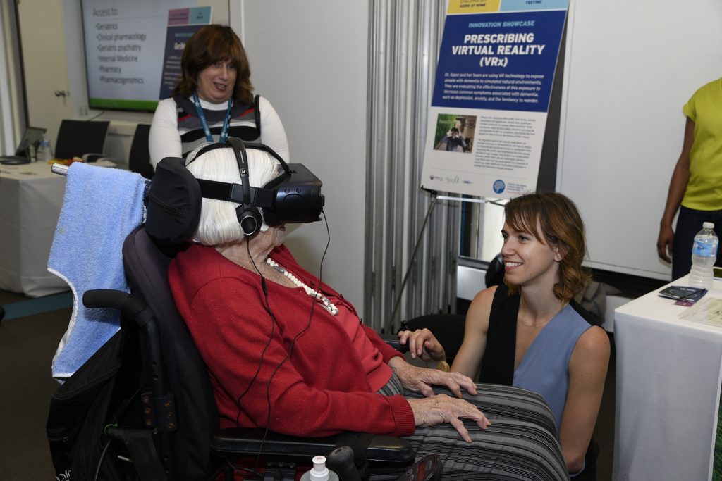 Laura Appel helps an older adult try a virtual reality headset during CABHI's Innovation Showcase.