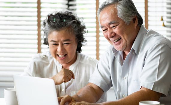 Two older adults laughing while using the computer.