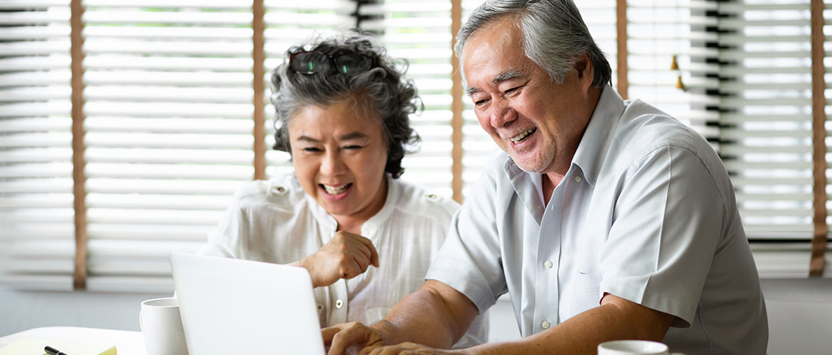 Two older adults laughing while using the computer.
