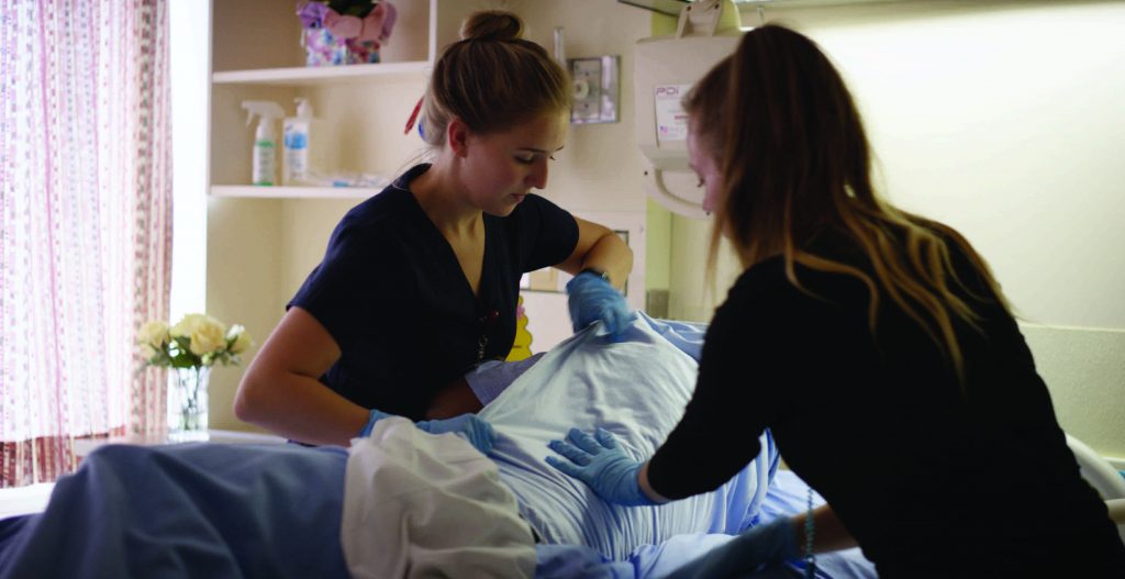 Two female nurses turning a patient in a hospital bed.