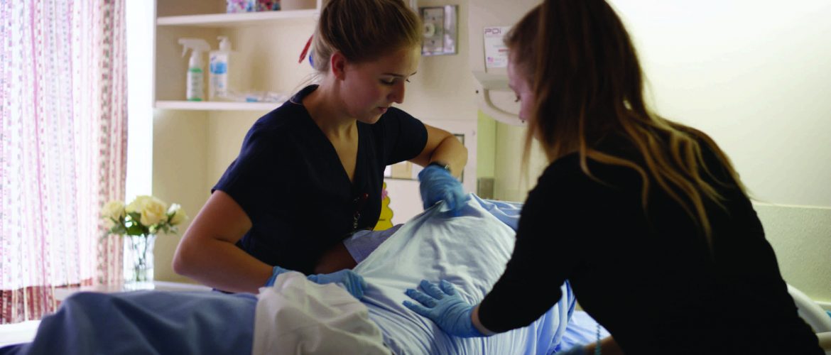 Two female nurses turning a patient in a hospital bed.