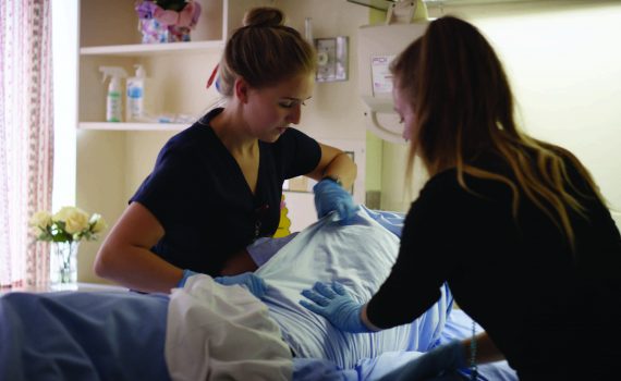 Two female nurses turning a patient in a hospital bed.