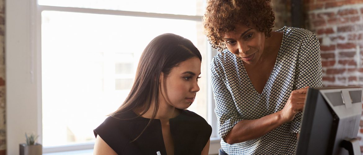A younger woman is helped by a senior colleague.