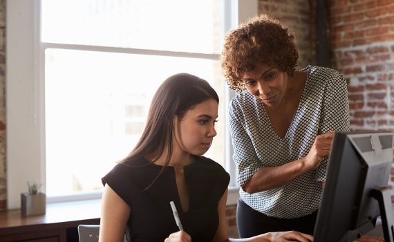 A younger woman is helped by her mentor.