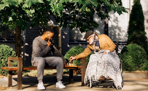 young man playing chess with older adult man in a park