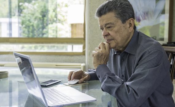 Latinx senior man working at home office with laptop computer.