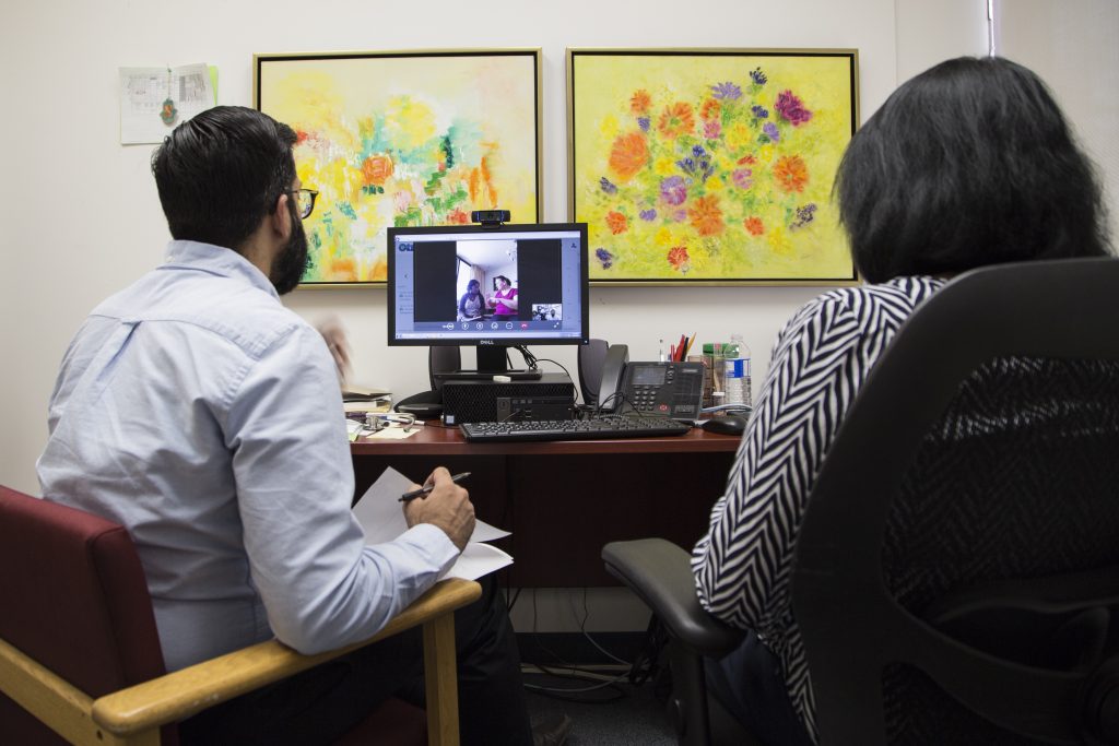 Two point-of-care workers deliver have a consult via a computer