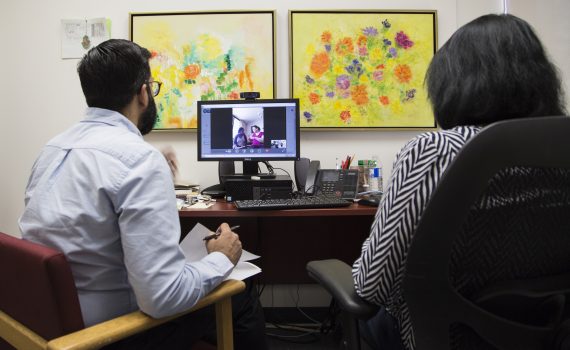 Two point-of-care workers deliver have a consult via a computer