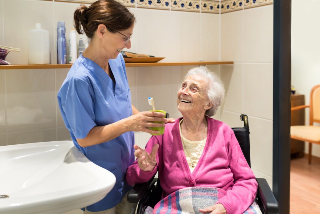 Point-of-care worker is talking with an older adult resident while holding a toothbrush in bathroom