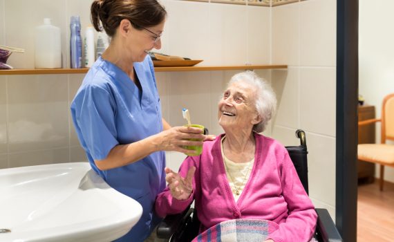 Point-of-care worker is talking with an older adult resident while holding a toothbrush in bathroom