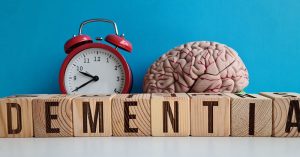 Wood blocks spelling out dementia. Red alarm clock. Brain model.