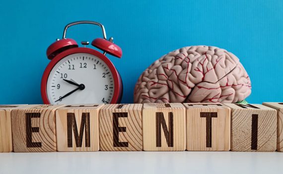 Wood blocks spelling out dementia. Red alarm clock. Brain model.