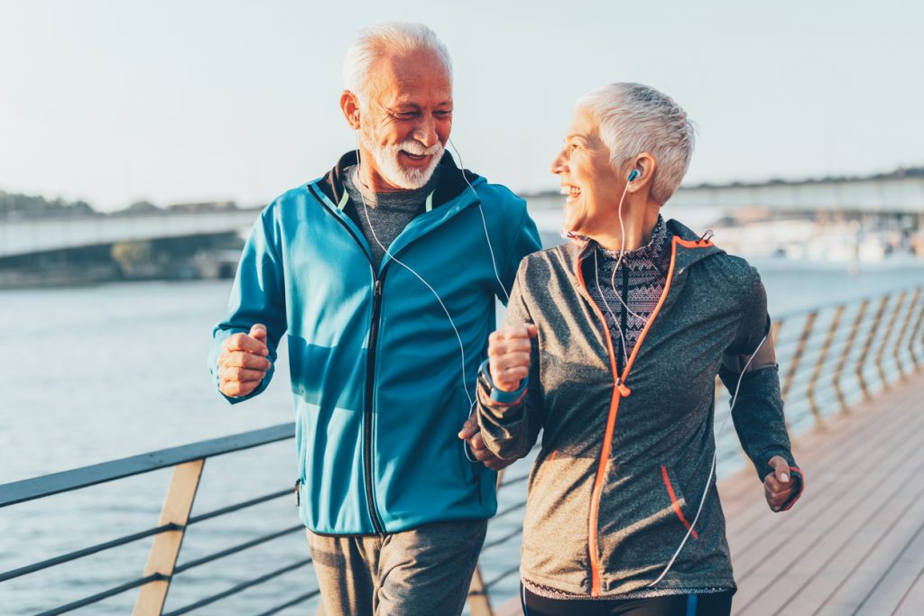 A senior man and woman power walking on a boardwalk and smiling