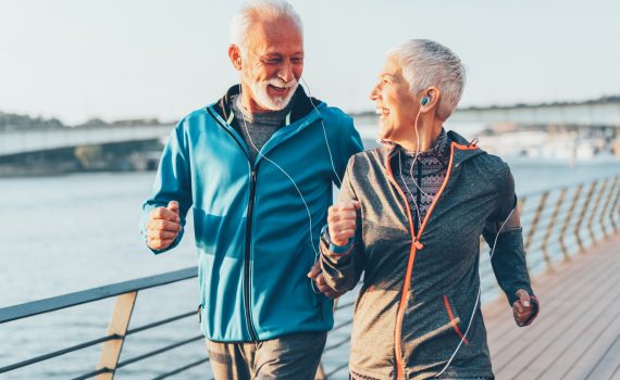A senior man and woman power walking on a boardwalk and smiling