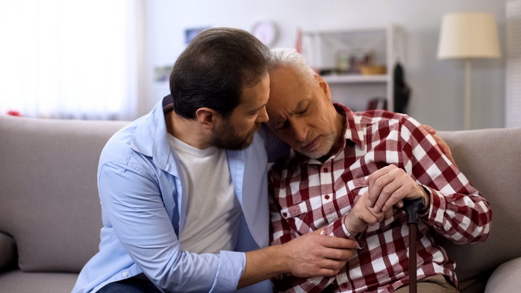 Middle aged son comforting senior father on couch