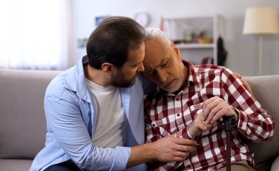 Middle aged son comforting senior father on couch