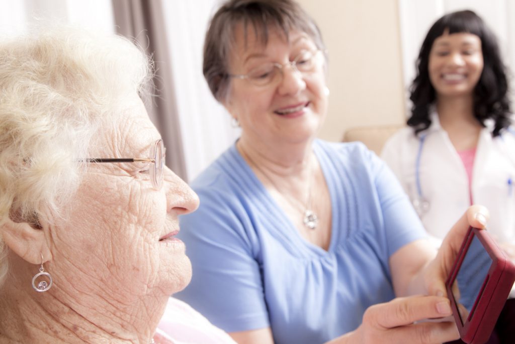Senior women use smartphone while point-of-care worker looks on