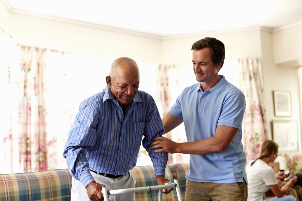 Point-of-care worker assisting a senior man to walk with a walker