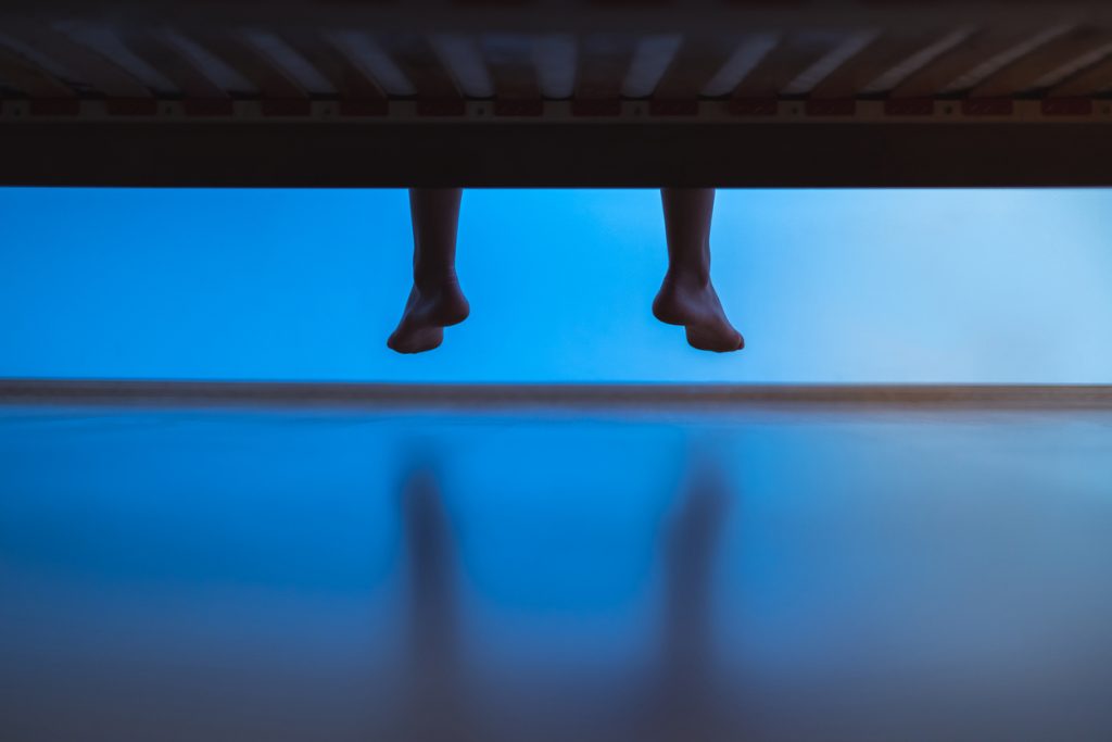 Legs dangling over the end of a bed at night