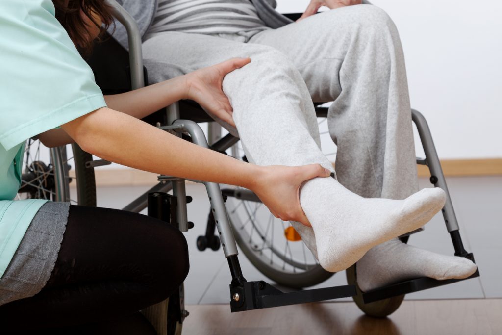 Point-of-care worker helps person in wheel chair perform leg movements.