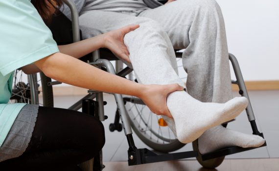 Point-of-care worker helps person in wheel chair perform leg movements.