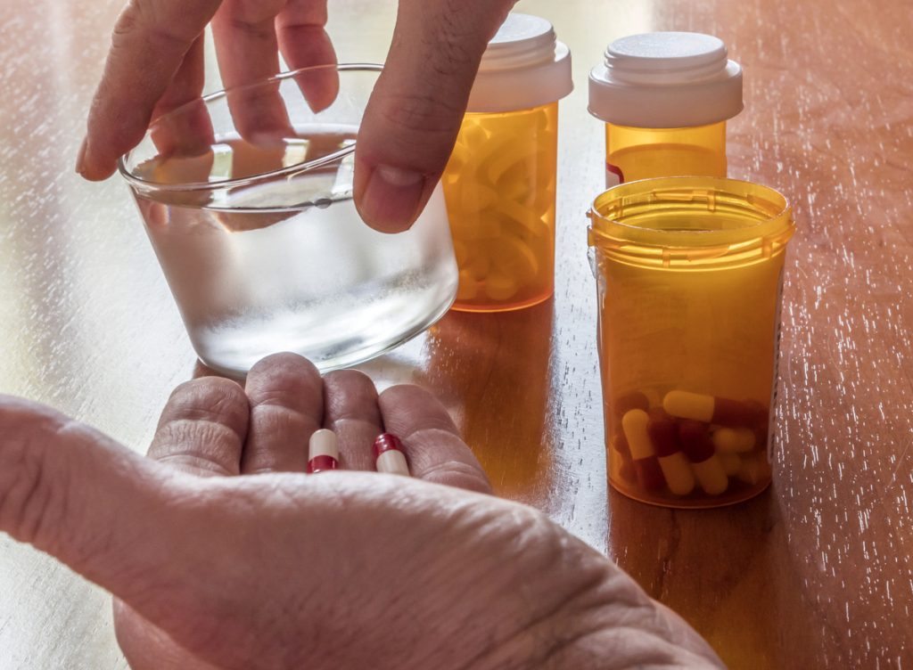 Hands holds a glass of water with medication bottles on the table.