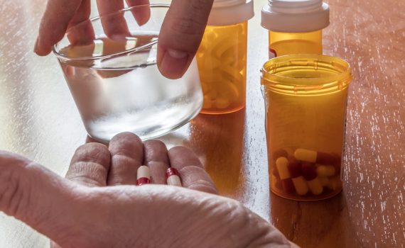 Hands holds a glass of water with medication bottles on the table.