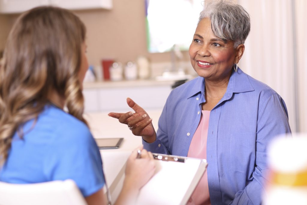 Doctor, mental health professional, or nurse gives medical advice or provides therapy to senior adult patient in office or clinic setting. She uses a tablet to record her notes or discuss test results. Medical exam, consultation, therapist.