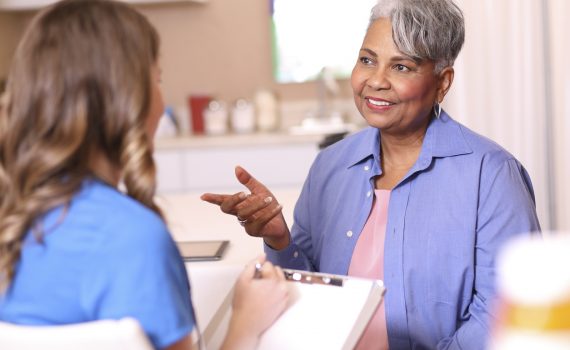 Doctor, mental health professional, or nurse gives medical advice or provides therapy to senior adult patient in office or clinic setting. She uses a tablet to record her notes or discuss test results. Medical exam, consultation, therapist.