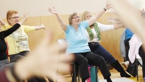 seniors seated in a room with arms outstretched