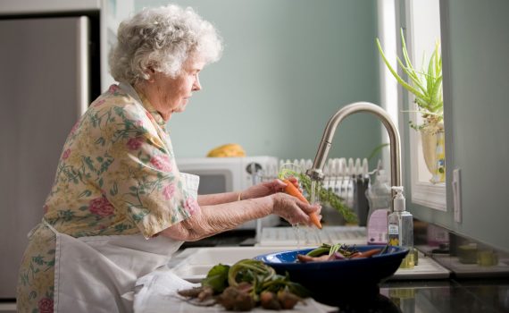 Older adult woman washing vegetables at her kitchen sink.