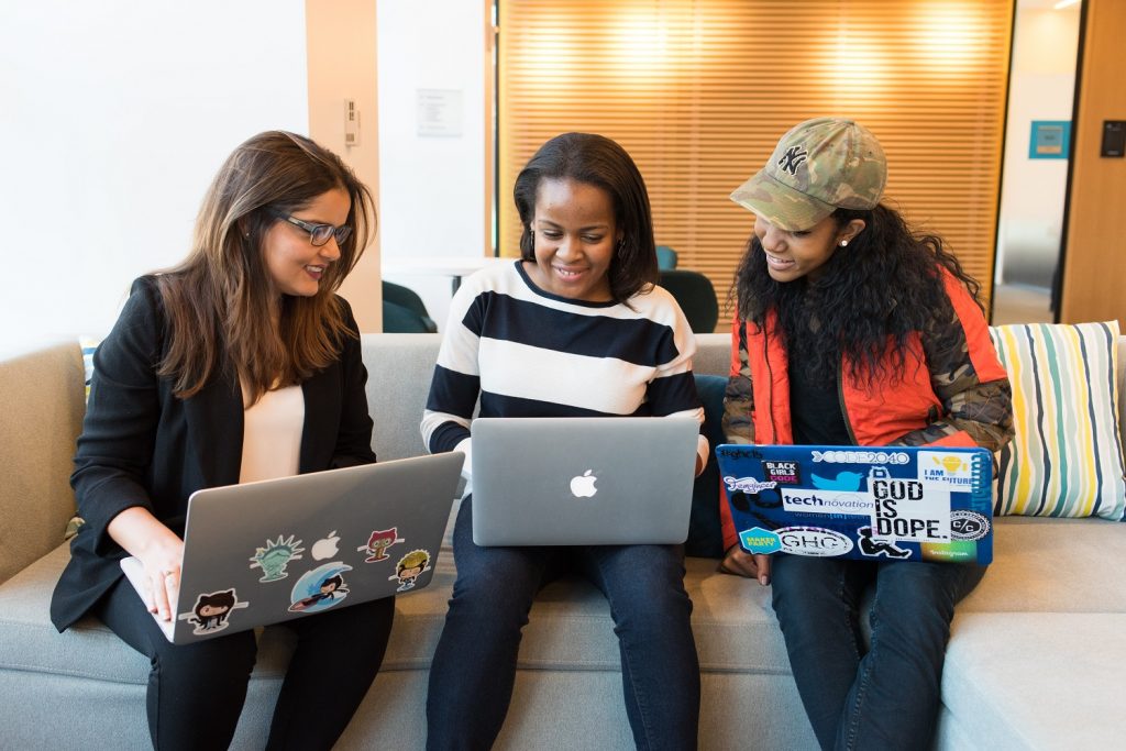 Three women sitting on a couch looking at laptops