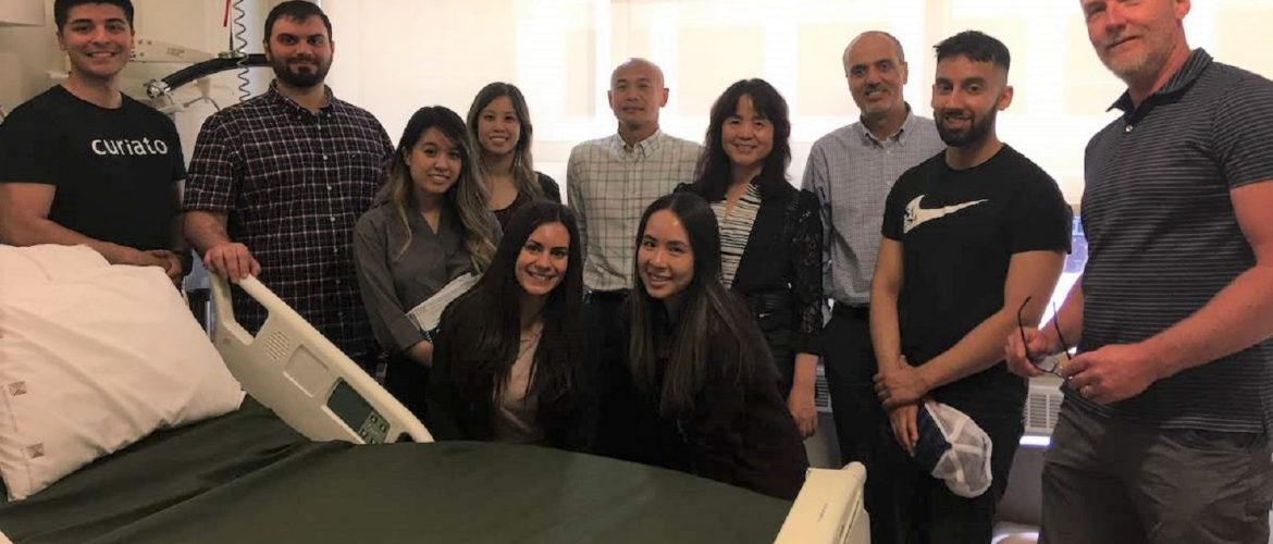 11 people standing around a hospital bed smiling.