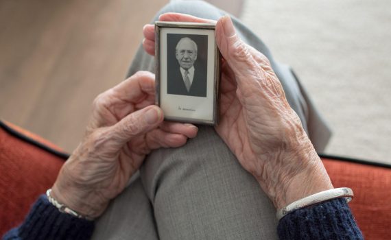An elderly pair of hands holds a "In memoriam" photo of a loved one.