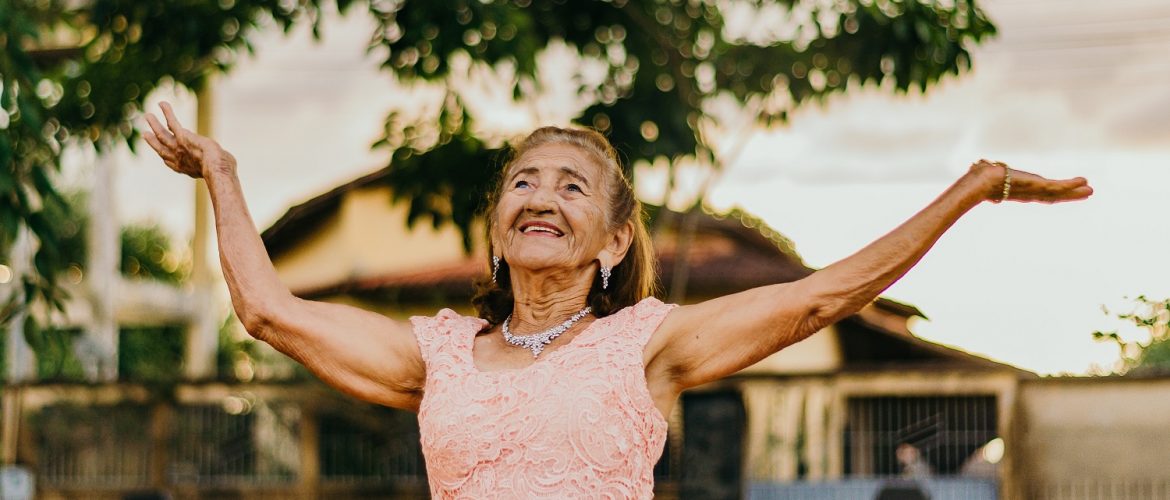 Older adult woman smiling with her arms raised in the air.