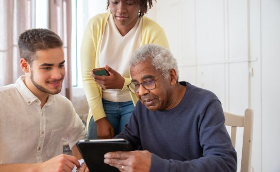 Two caretakers helping an older adult man with tablet