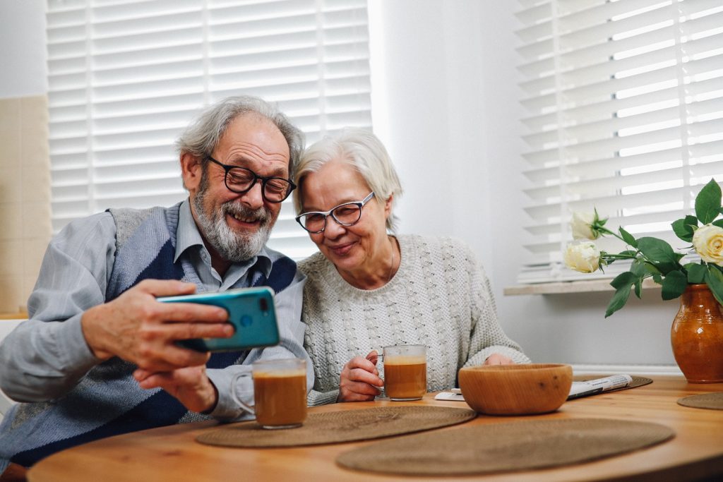 An older man and woman smiling into a phone