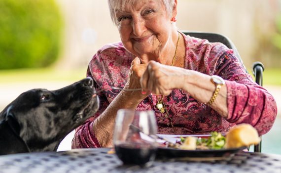 Older adult woman eating with a dog beside her