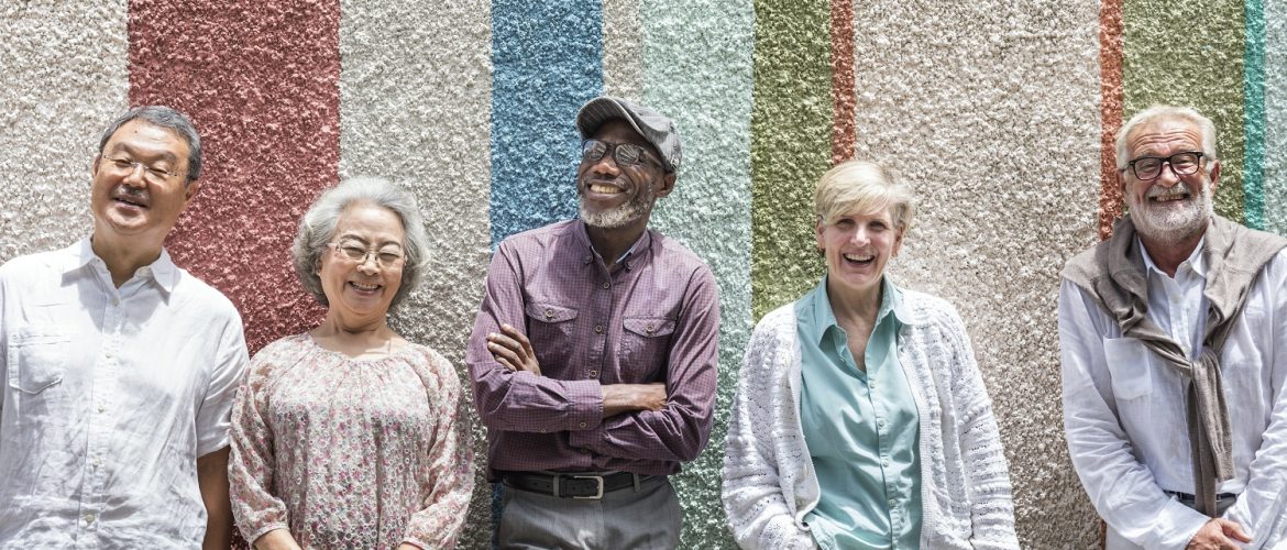 A group of diverse seniors stand up against a multi-coloured wall