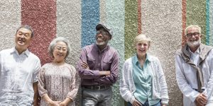 A group of diverse seniors stand up against a multi-coloured wall